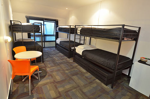 Image of accommodation at Base with 3 bunk beds with black quilts and orange chairs