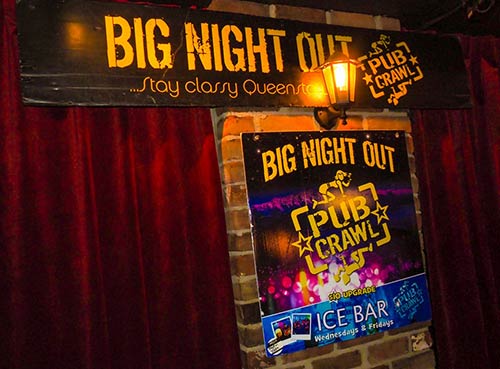 Signage of Big Night Out pub crawl with red curtain behind