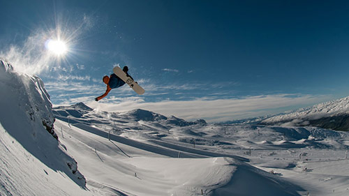 Mid air shot of guy on snowboard. Sun in background
