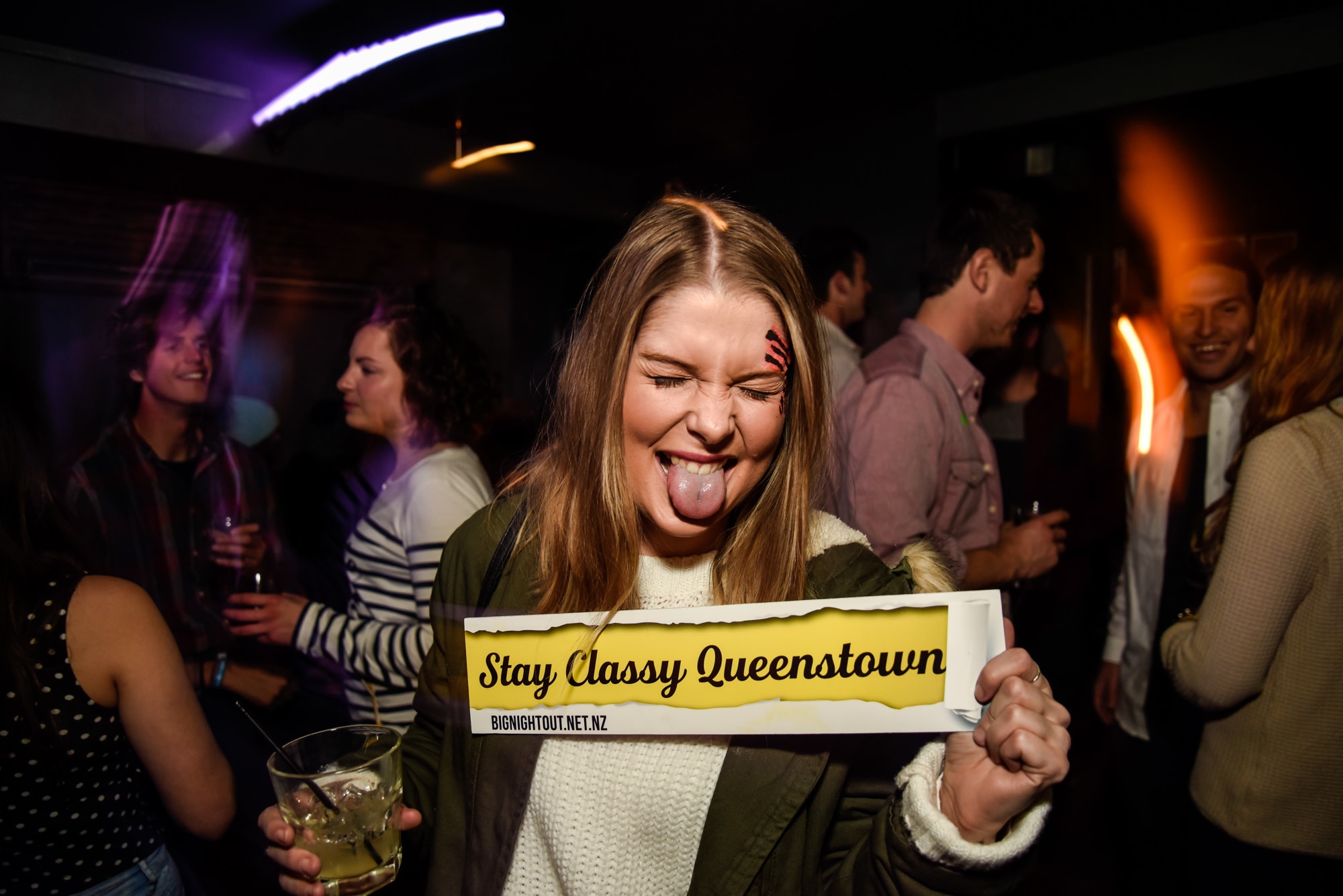 Girl sticking out her tongue having fun on the big night out pub crawl in Queenstown with stay classy Queenstown sign