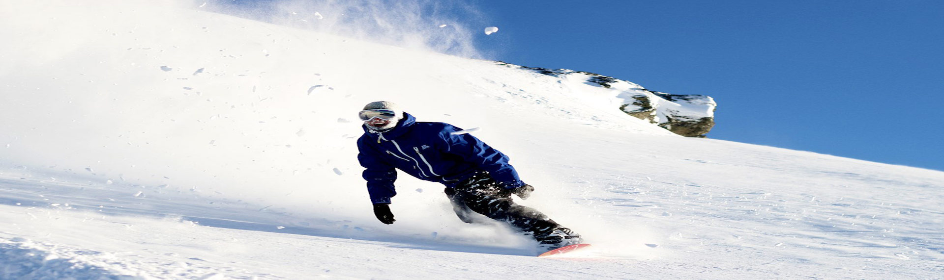 Guy wearing blue jacket snowboarding down snow slope